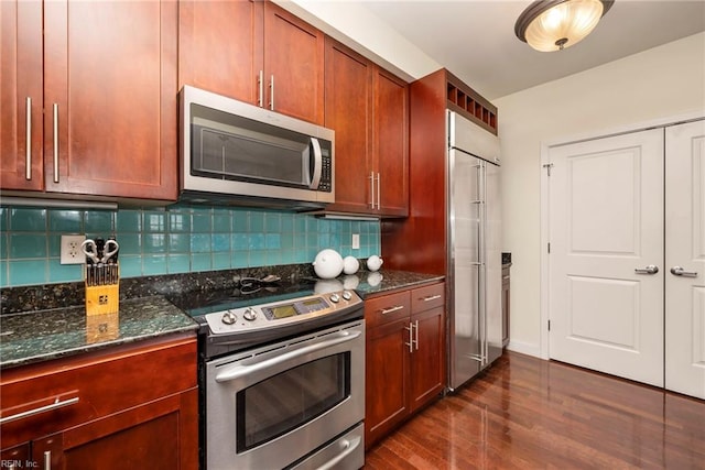 kitchen featuring appliances with stainless steel finishes, dark wood-style flooring, dark stone countertops, and tasteful backsplash