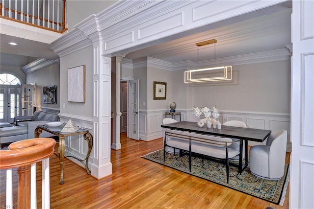 dining area with a wainscoted wall, ornamental molding, and light wood-type flooring