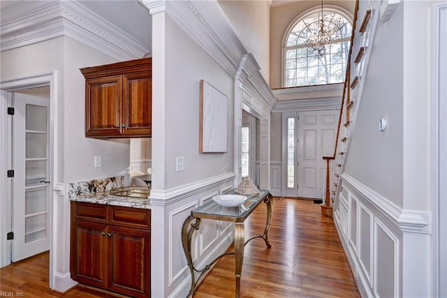 entrance foyer featuring wainscoting, stairway, wood finished floors, a decorative wall, and a notable chandelier