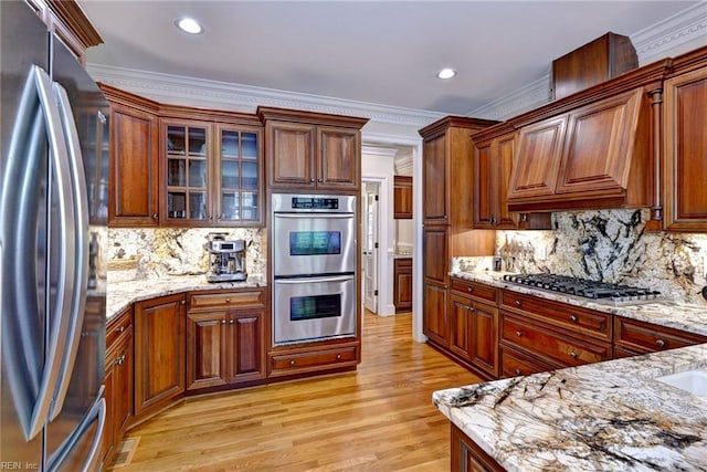 kitchen with light stone countertops, tasteful backsplash, appliances with stainless steel finishes, and light wood-style floors