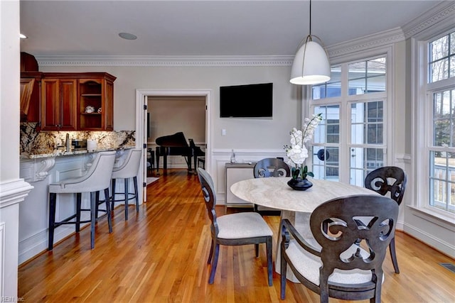 dining area with a wainscoted wall, visible vents, crown molding, and light wood finished floors