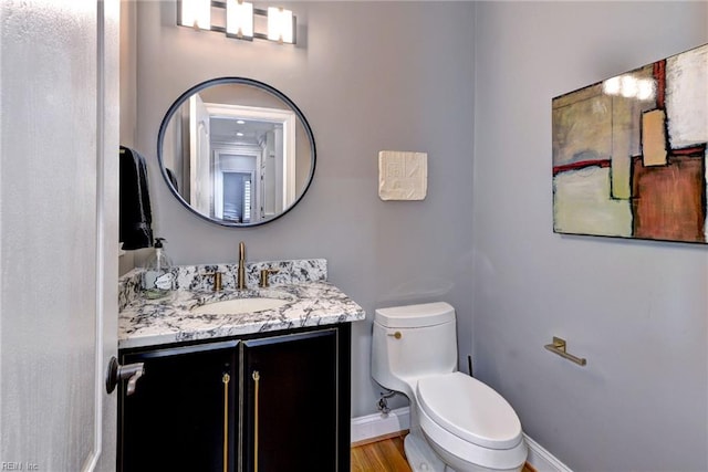 half bathroom with baseboards, vanity, toilet, and wood finished floors