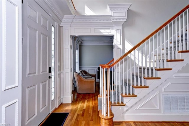 foyer with light wood-type flooring, stairs, ornamental molding, and a decorative wall