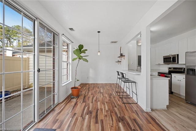 kitchen featuring light wood-style flooring, stainless steel appliances, visible vents, white cabinets, and light countertops