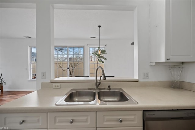 kitchen with light countertops, visible vents, stainless steel dishwasher, white cabinets, and a sink