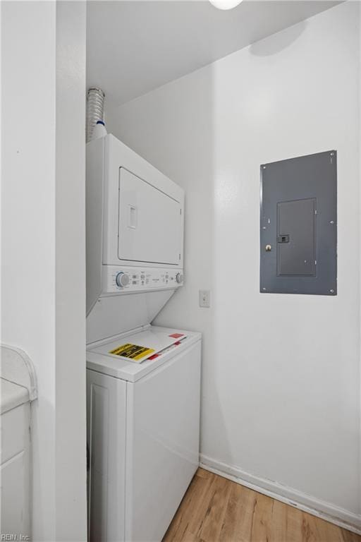 laundry area featuring laundry area, electric panel, baseboards, stacked washer / drying machine, and light wood-type flooring