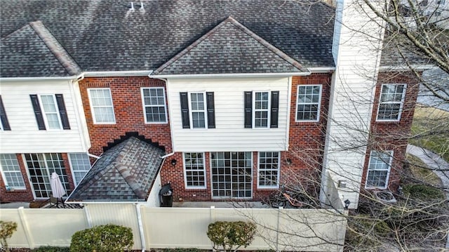 view of front of house featuring a shingled roof, brick siding, and a fenced front yard