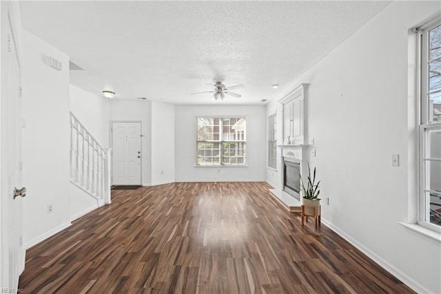 unfurnished living room with a textured ceiling, dark wood-type flooring, a fireplace, and baseboards