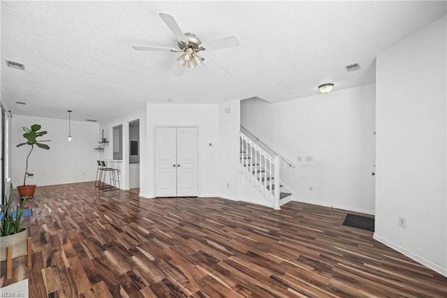 unfurnished living room featuring visible vents, a textured ceiling, stairway, and wood finished floors