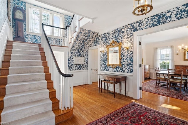 foyer with light wood-type flooring, wallpapered walls, a notable chandelier, and wainscoting