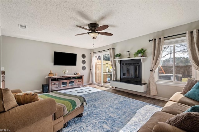 living room featuring ceiling fan, wood finished floors, visible vents, baseboards, and a glass covered fireplace