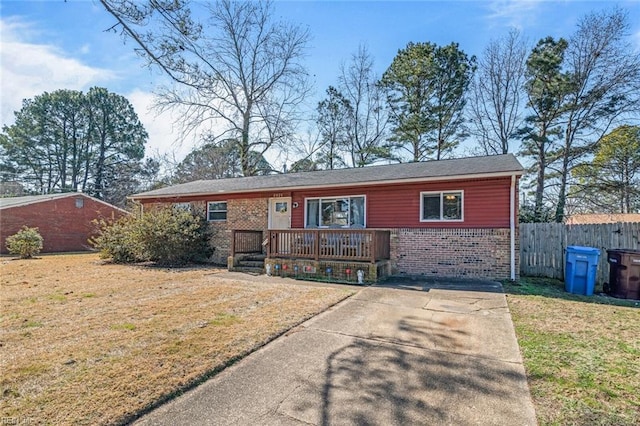 ranch-style home with covered porch, brick siding, fence, and a front lawn