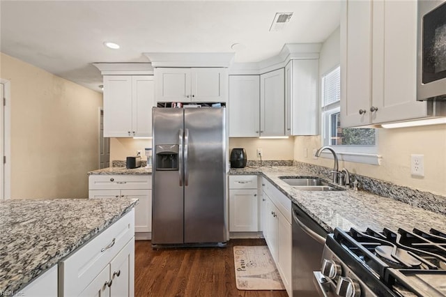 kitchen featuring white cabinets, light stone counters, dark wood-style flooring, stainless steel appliances, and a sink