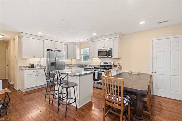 kitchen with white cabinetry, a kitchen bar, appliances with stainless steel finishes, and dark wood-style flooring