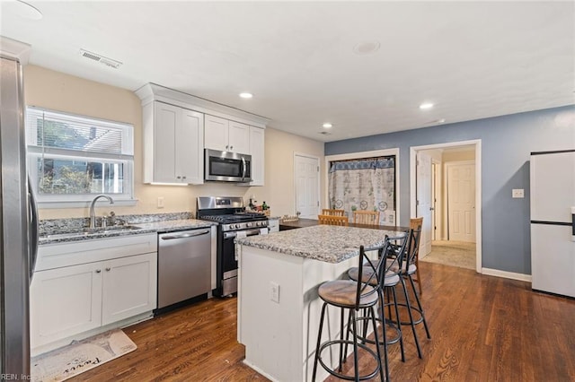 kitchen featuring a center island, stainless steel appliances, visible vents, a sink, and light stone countertops