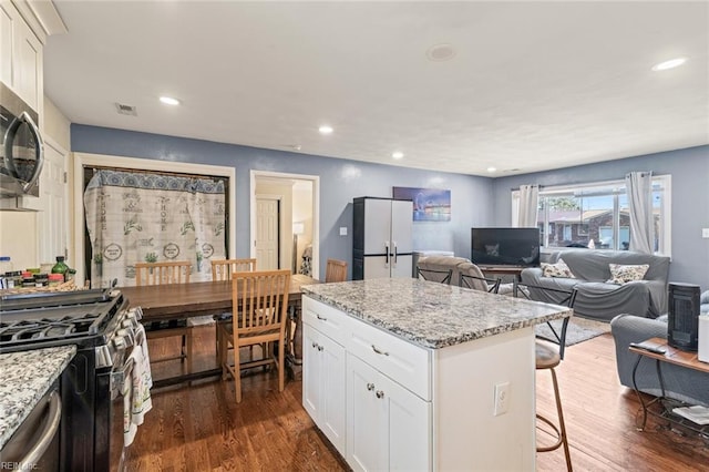 kitchen with a breakfast bar area, stainless steel appliances, a kitchen island, white cabinets, and dark wood finished floors