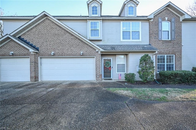 multi unit property featuring a garage, driveway, brick siding, and roof with shingles