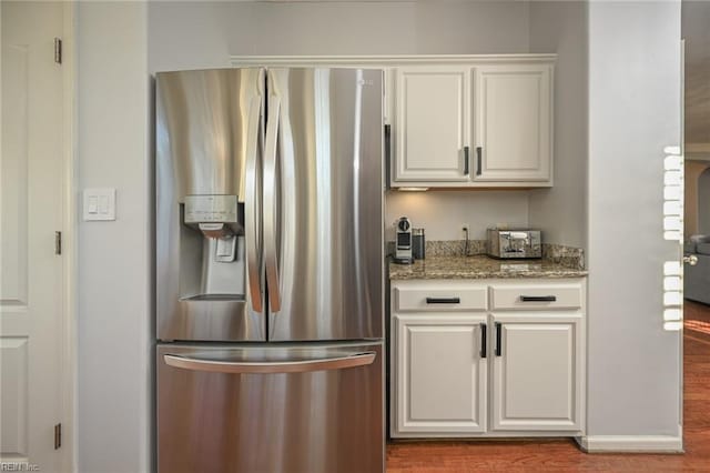 kitchen with light stone counters, stainless steel refrigerator with ice dispenser, white cabinets, wood finished floors, and baseboards