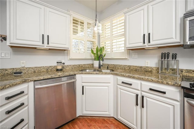 kitchen featuring light wood-style flooring, stainless steel appliances, a sink, white cabinets, and decorative light fixtures