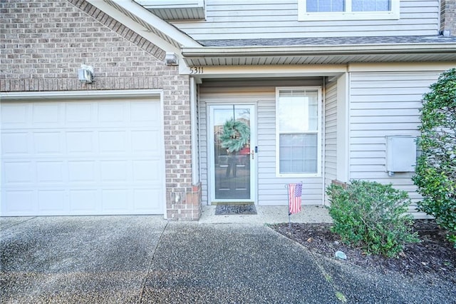 doorway to property with an attached garage, driveway, and brick siding