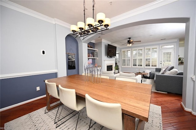 dining area with arched walkways, a fireplace, crown molding, and wood finished floors