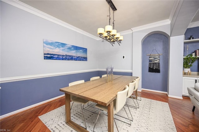 dining space with arched walkways, an inviting chandelier, ornamental molding, wood finished floors, and baseboards