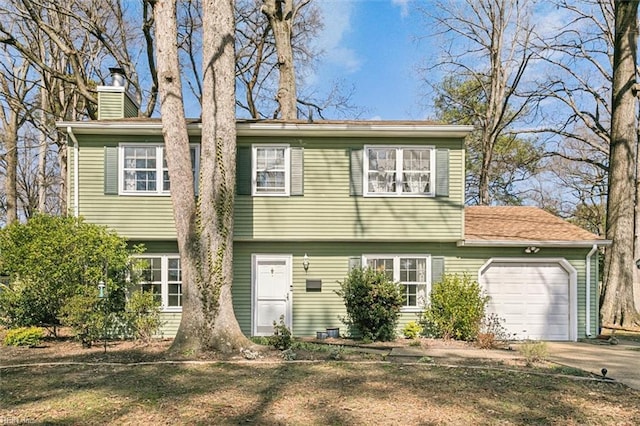 colonial house featuring an attached garage, a chimney, and concrete driveway