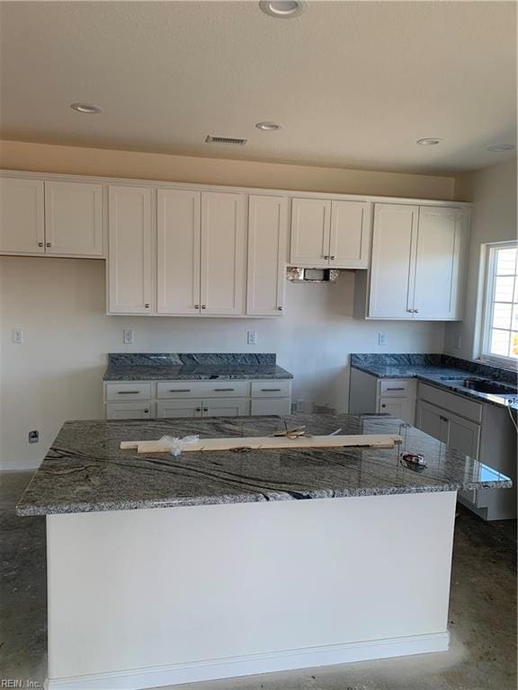 kitchen featuring stone counters, white cabinets, visible vents, and a kitchen island