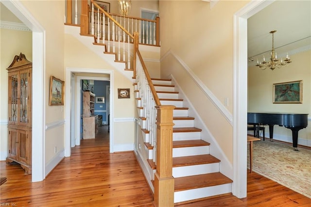 stairway featuring baseboards, wood finished floors, a towering ceiling, and an inviting chandelier