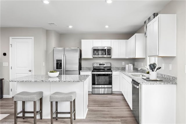 kitchen featuring visible vents, a kitchen island, appliances with stainless steel finishes, a breakfast bar area, and white cabinetry