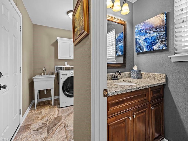 clothes washing area with cabinet space, a textured wall, a sink, washer / dryer, and baseboards