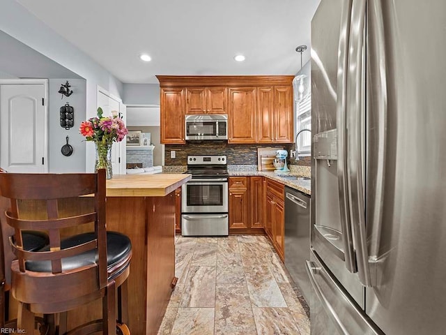 kitchen with a sink, wood counters, appliances with stainless steel finishes, backsplash, and brown cabinets