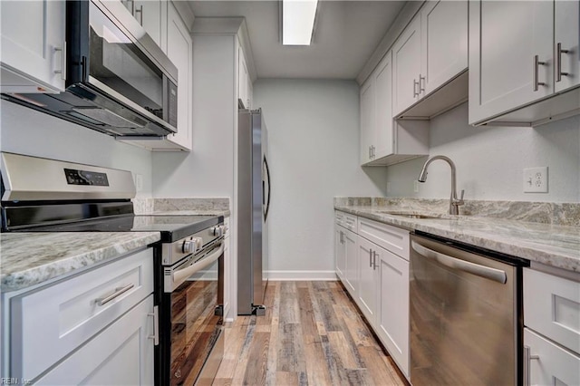 kitchen featuring stainless steel appliances, a sink, baseboards, light wood-type flooring, and light stone countertops