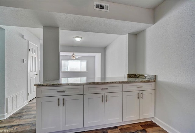 kitchen with a peninsula, visible vents, dark wood-style flooring, and light stone counters