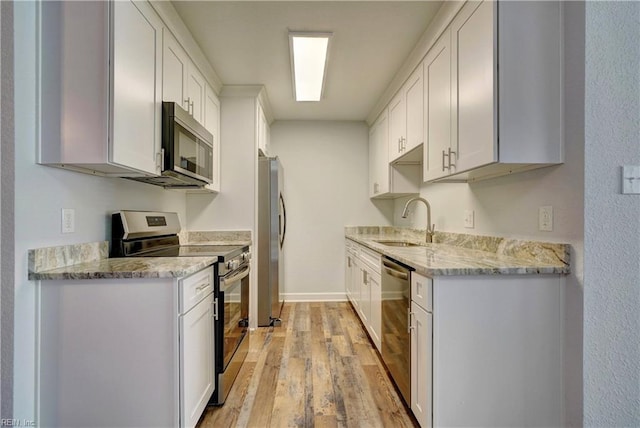 kitchen featuring light stone counters, light wood-style flooring, appliances with stainless steel finishes, white cabinetry, and a sink