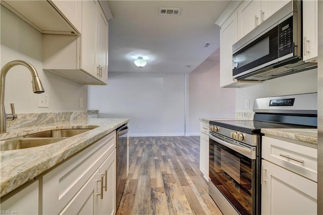 kitchen with light wood finished floors, white cabinets, appliances with stainless steel finishes, light stone countertops, and a sink