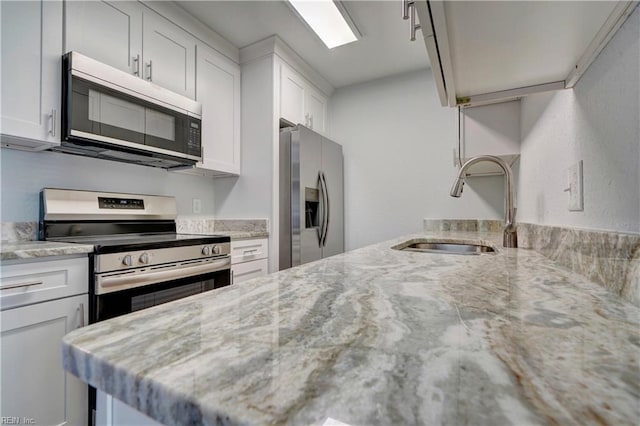 kitchen with appliances with stainless steel finishes, a sink, white cabinetry, and light stone countertops