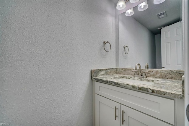 bathroom featuring a textured wall, vanity, and visible vents