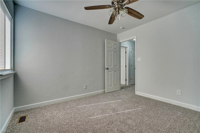 unfurnished bedroom featuring baseboards, visible vents, a ceiling fan, a textured wall, and carpet floors