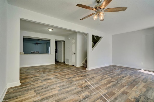 empty room featuring visible vents, stairway, a ceiling fan, wood finished floors, and baseboards