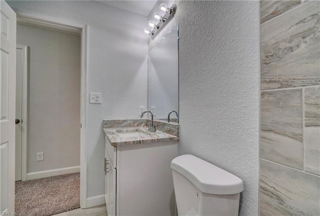 bathroom featuring toilet, vanity, baseboards, and a textured wall