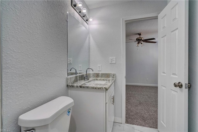 half bath featuring marble finish floor, a textured wall, toilet, ceiling fan, and vanity