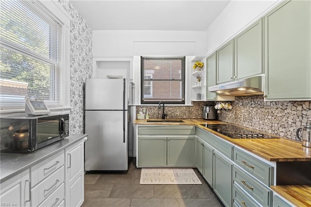 kitchen featuring butcher block counters, freestanding refrigerator, under cabinet range hood, green cabinets, and a sink