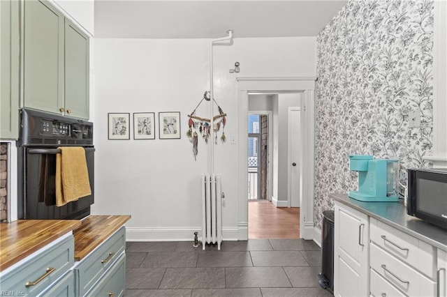 kitchen featuring butcher block countertops, dark tile patterned flooring, baseboards, black appliances, and radiator heating unit