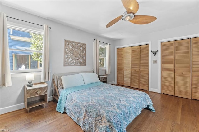 bedroom featuring a ceiling fan, wood finished floors, baseboards, and two closets