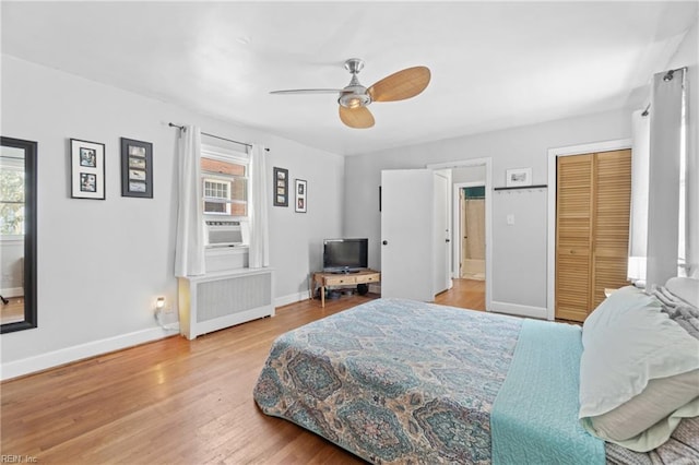 bedroom featuring radiator, multiple windows, baseboards, and wood finished floors