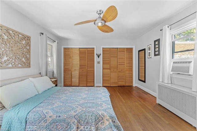 bedroom featuring cooling unit, baseboards, multiple closets, light wood-type flooring, and radiator