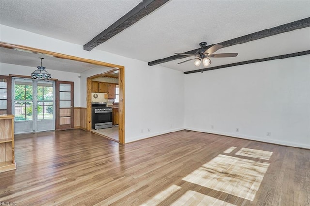 unfurnished living room featuring beam ceiling, ceiling fan, a textured ceiling, wood finished floors, and baseboards