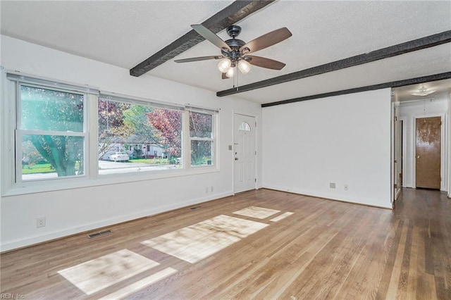 spare room featuring visible vents, a textured ceiling, wood finished floors, beamed ceiling, and baseboards