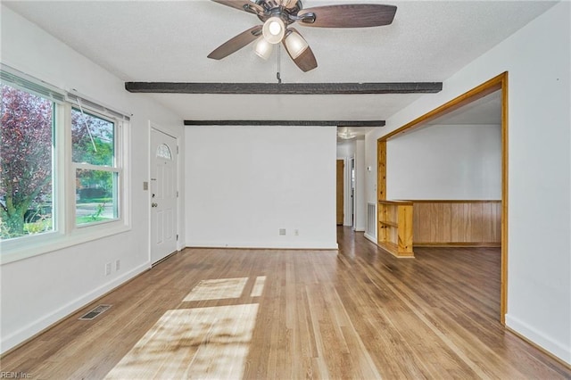 spare room featuring a textured ceiling, wood finished floors, visible vents, baseboards, and beam ceiling